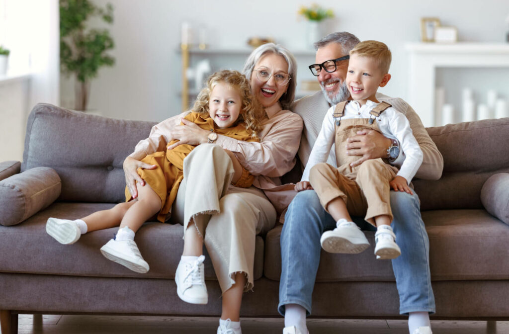 Little children visiting, hugging, and embracing grandparents while sitting together on a sofa in the living room .