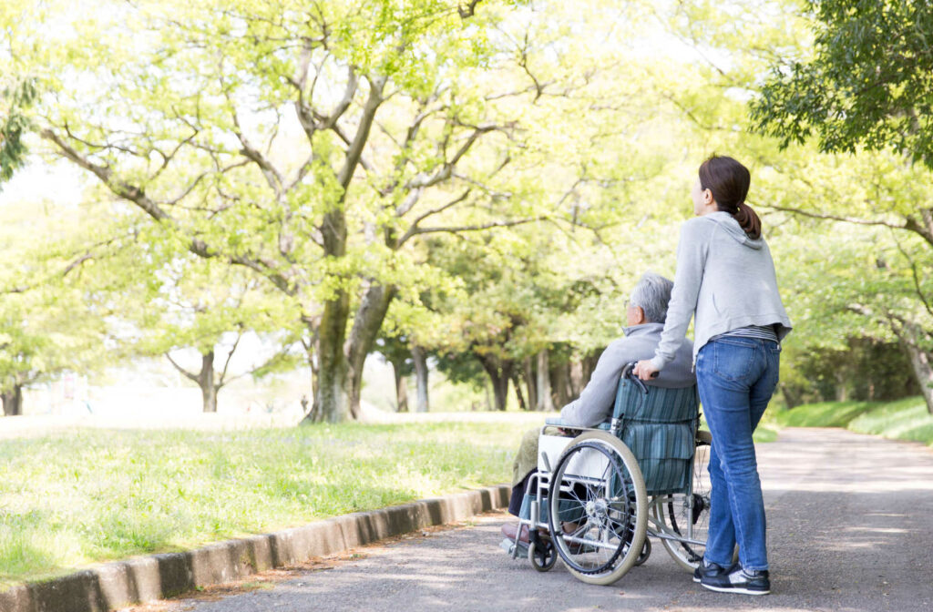 A young woman helping her father in a wheelchair have a nice time outside in a park.
