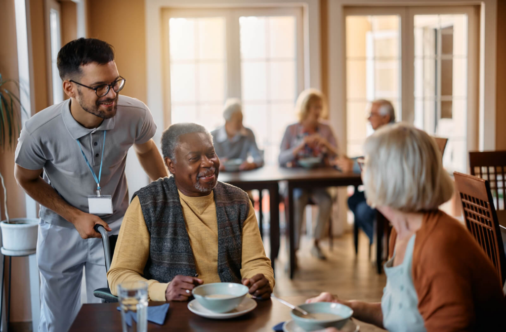 A group of happy senior people engaged in conversation with their caregiver in a home setting.