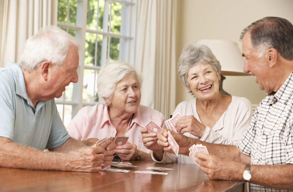 A group of seniors gathered around a table talking, smiling and playing cards