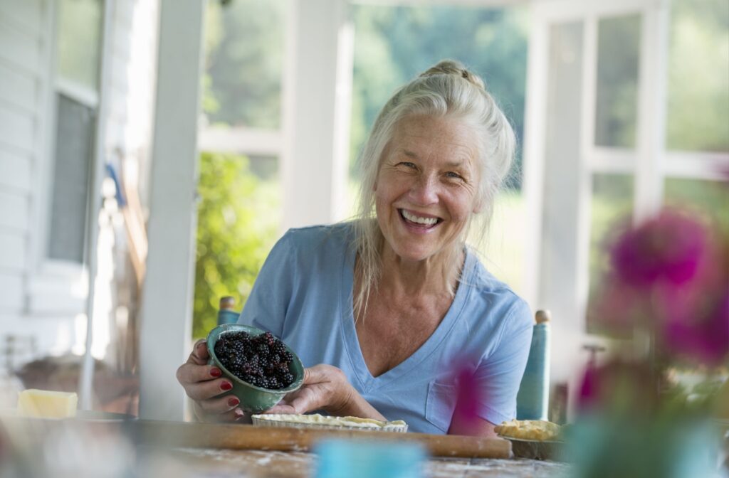 An older adult woman holding a bowl of blackberries smiling and looking directly at the camera