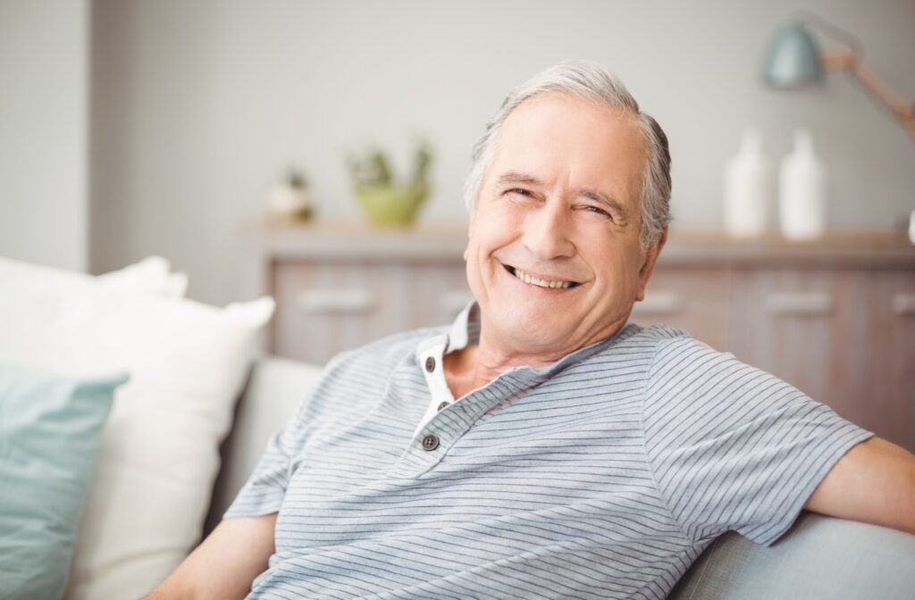 A senior man sitting on a couch smiling and looking directly at the camera