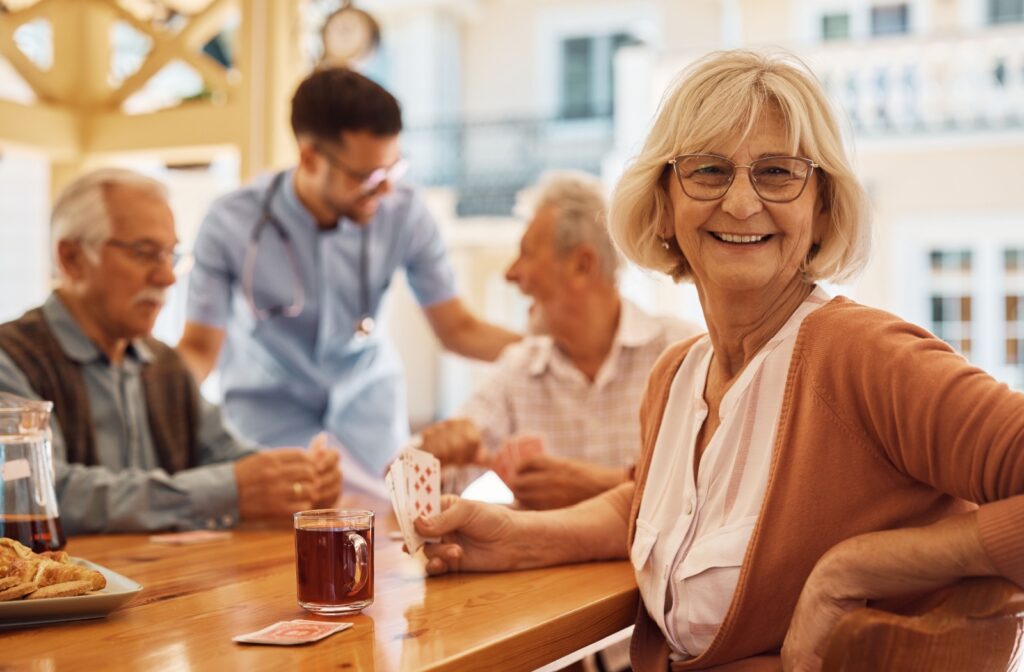 Group of seniors playing cards with a caregiver, while a smiling elderly woman holds a hand of cards