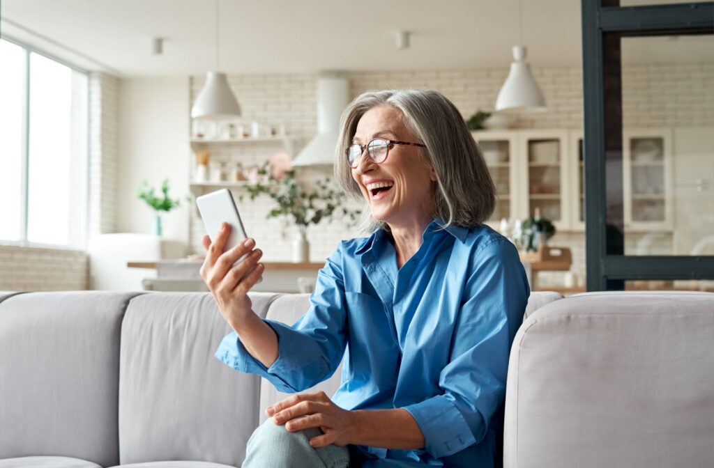 A senior woman happily video chatting with her family on her smartphone from her home at a senior living community.