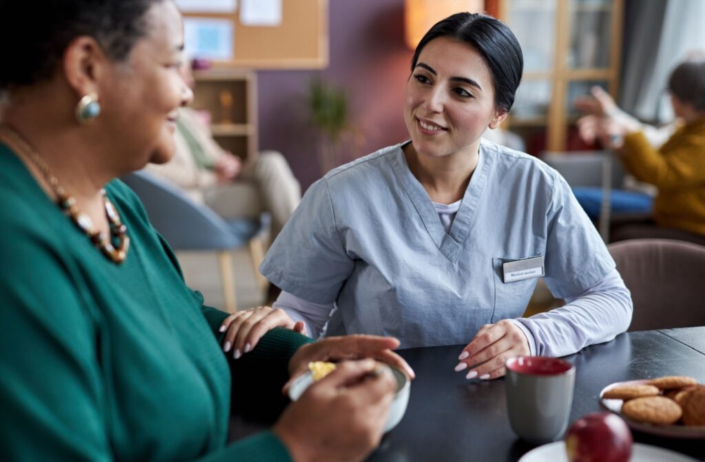 A community nurse and resident sit together over tea and snacks in the dining room.