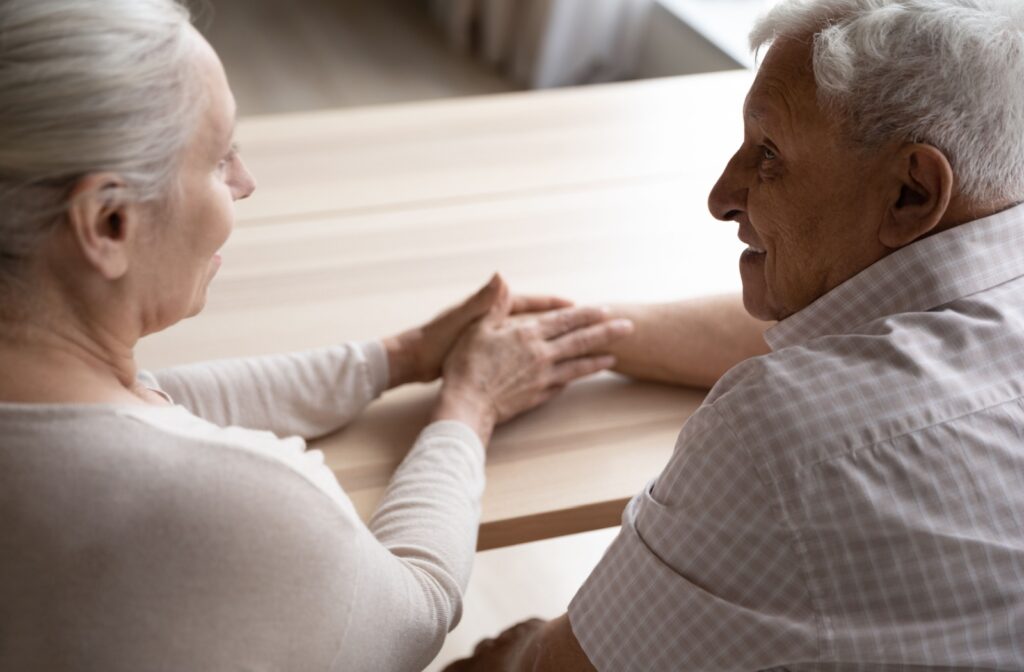 Over-the-shoulder shot of a middle-aged woman and an older senior man holding hands on a table.