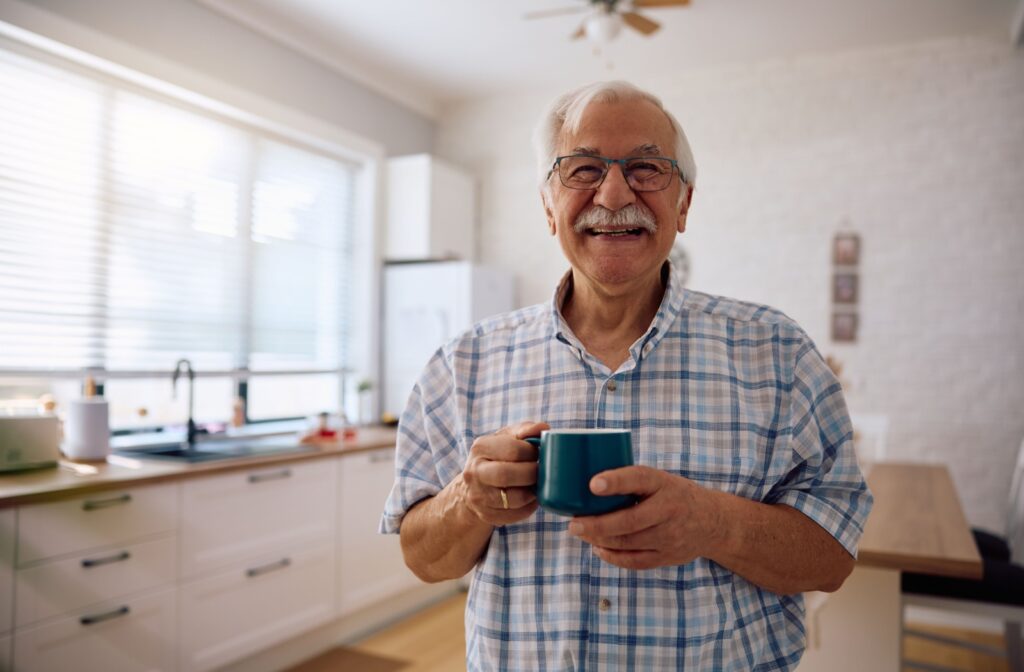 A smiling senior holds a mug of coffee to enjoy first thing in the morning in their assisted living home