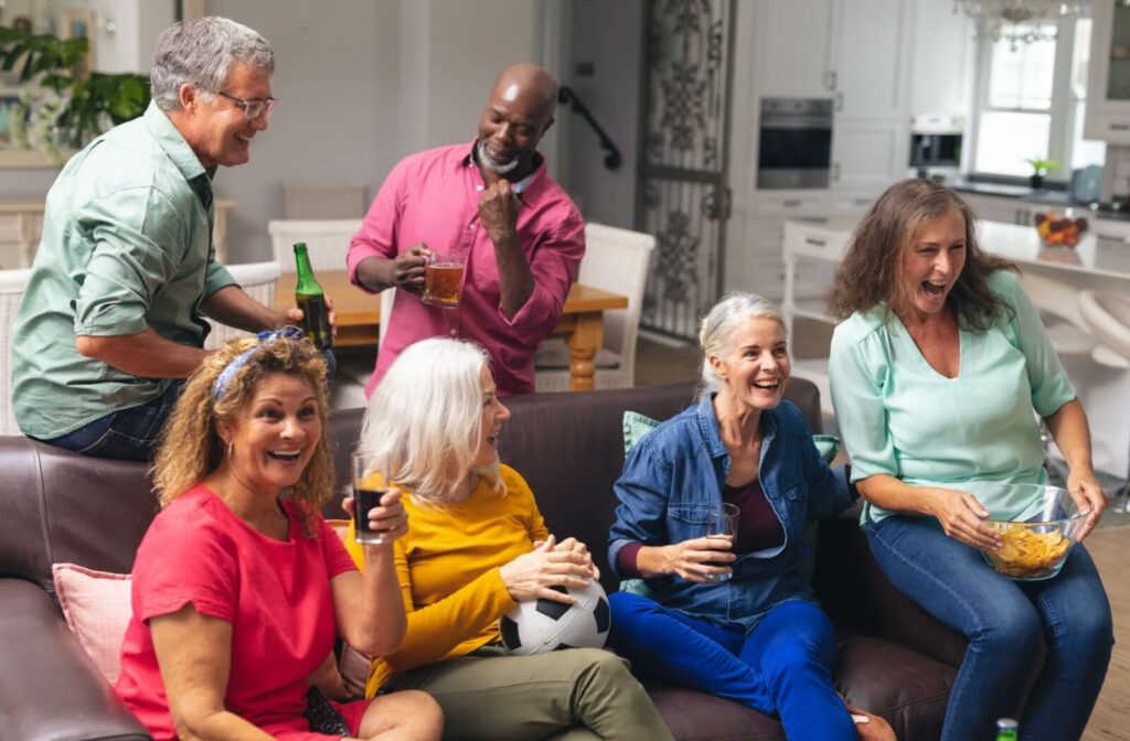 A group of seniors gather in a shared living space to socialize and watch a game on TV in a senior living community