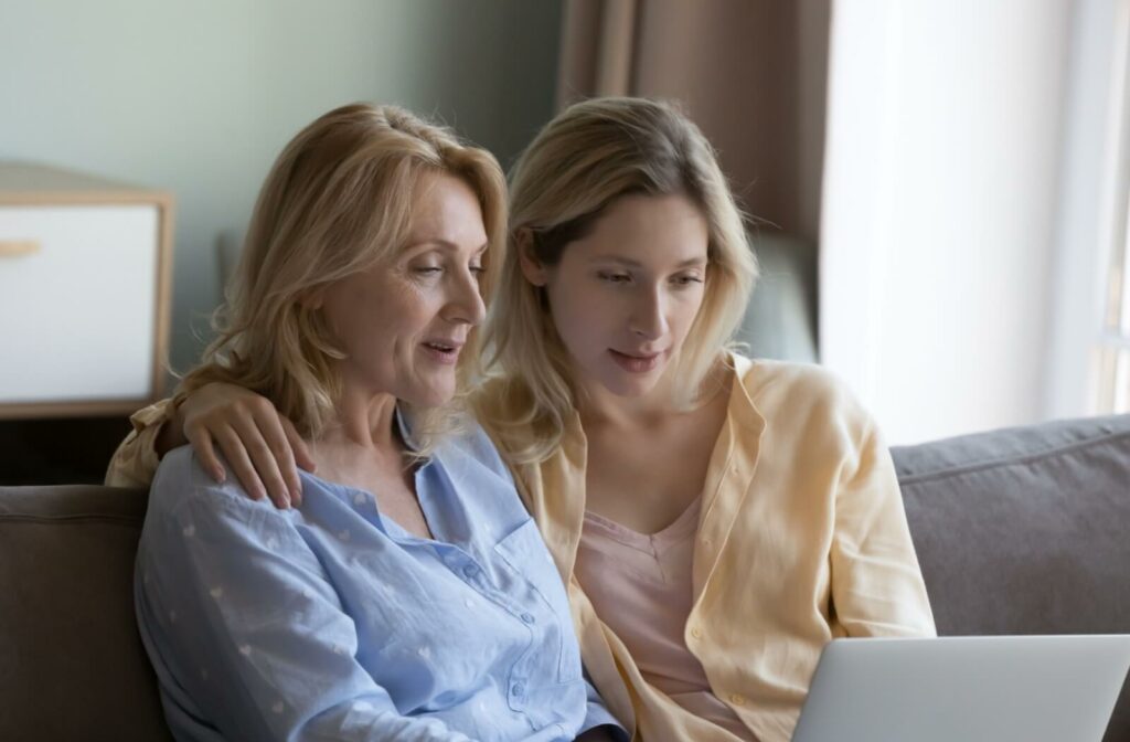 An adult has their arm over their older parent’s shoulders while they research assisted living communities together