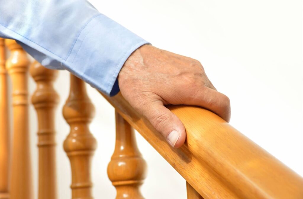A close-up image of an older adult's hand gripping a wooden banister to walk safely down the stairs