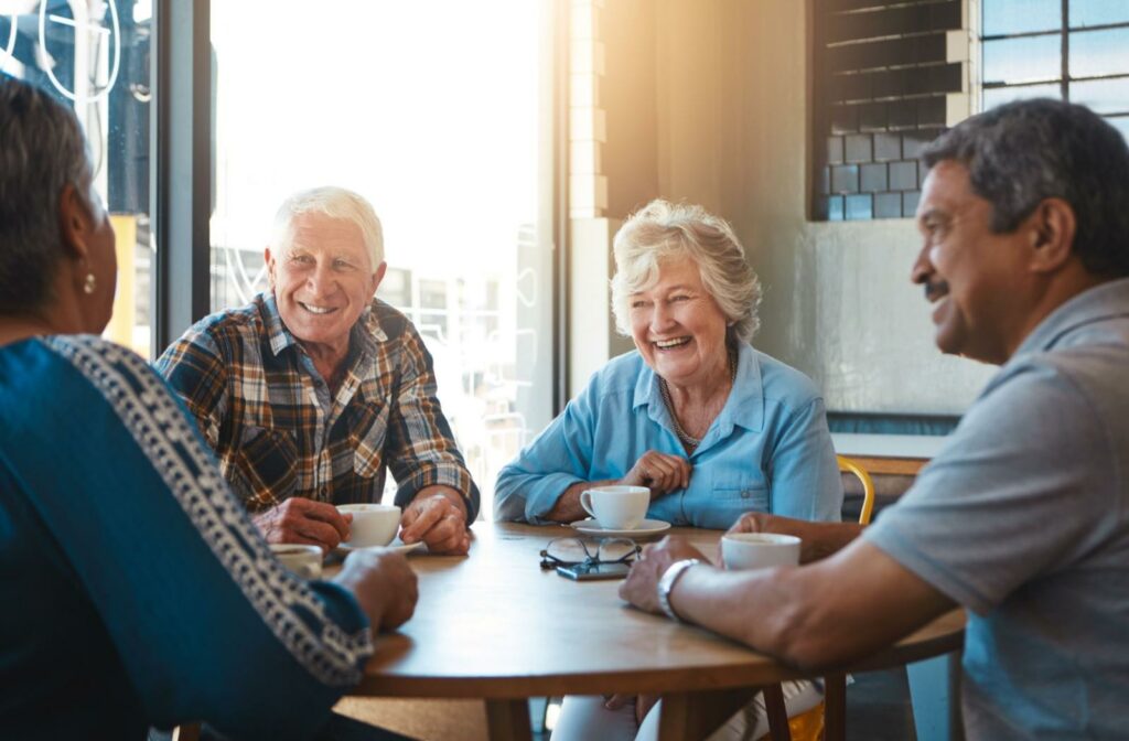 A group of seniors smiling and talking together in a brightly lit common lounge area.